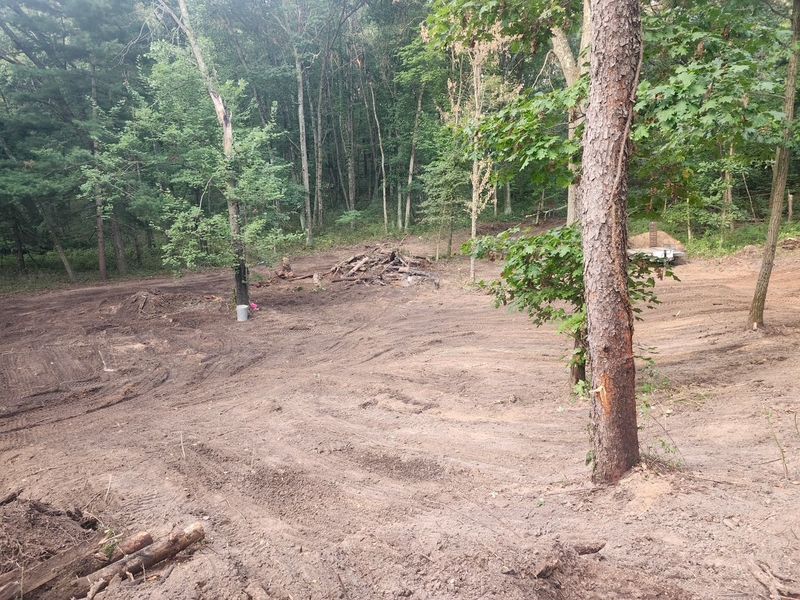Freshly cleared and graded dirt lot surrounded by mature trees in Holmen, Wisconsin